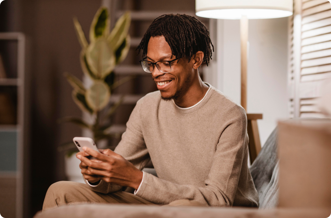 Home negro com moletom bege mexendo no celular e sorrindo